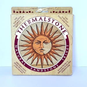 Könnte beinhalten: Ein quadratischer, natürlicher Sandstein-Topfuntersetzer mit einem Sonnendesign. Hergestellt aus 75 Millionen Jahre altem Sandstein, absorbiert er Tropfen von Getränken. Die Verpackung trägt die Aufschrift "Thermalstone Trivet".