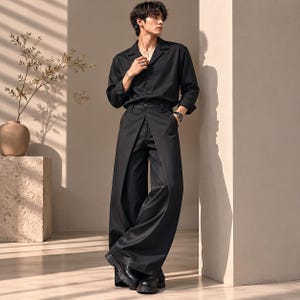 May include: A black long-sleeved button-down shirt with a notched collar paired with black wide-leg trousers featuring a distinct front overlay panel. The ensemble is completed with black leather boots, creating a monochromatic look.