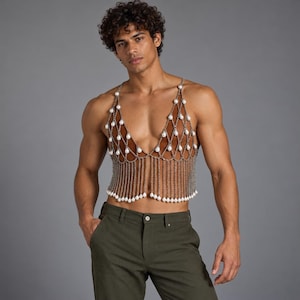 May include: A brown velvet halter top featuring a decorative silver chain mesh overlay. The mesh is adorned with white teardrop-shaped faux pearls at each intersection and along the bottom fringe, creating a structured, layered appearance.