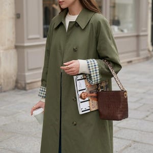 May include: A white ceramic mug with a black handle and the text "But First, Coffee" in a bold, black font. The mug is set against a blurred background, suggesting a cozy setting.