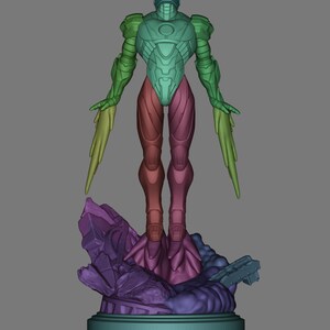 May include: A multi-colored figurine of a humanoid robot with outstretched arms and stylized wings. The robot is standing on a purple and blue rocky base. The robot's body is a gradient of green, blue, and red.