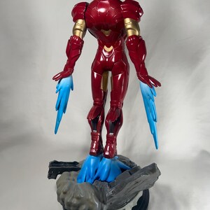 May include: A red and gold Iron Man action figure with blue energy effects emanating from the hands and feet. The figure is standing on a gray and black base. The figure is approximately 12 inches tall.