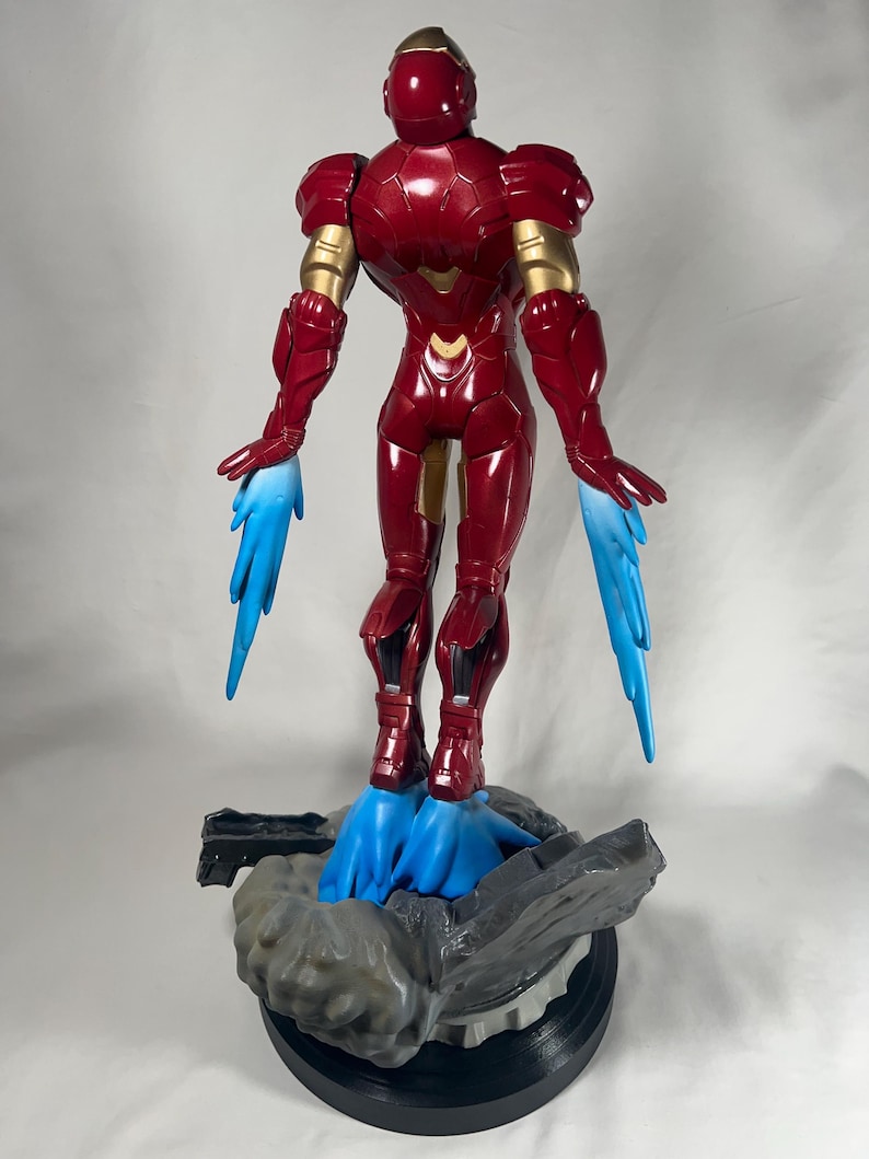 May include: A red and gold Iron Man action figure with blue energy effects emanating from the hands and feet. The figure is standing on a gray and black base. The figure is approximately 12 inches tall.