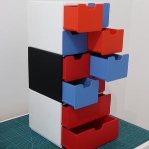 Può includere: Unità di stoccaggio multicolore con cornice bianca, accento nero e cassetti rossi e blu. I cassetti sono parzialmente estratti. L'unità è su un tappetino da taglio verde.