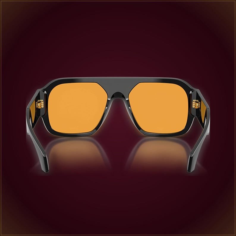 May include: Sunglasses featuring a thick, glossy black frame with a flat top bar and a bridge that connects the two lenses. The lenses are a vibrant, solid orange color. The hinges on the sides of the frame are visible and metallic in appearance.