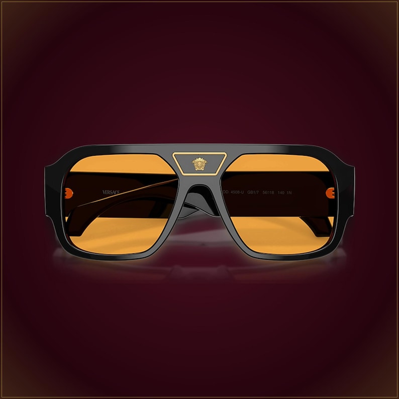 May include: Black sunglasses with a thick frame and orange-tinted lenses. A gold-tone Medusa head emblem is centered on the bridge. The frame features a flat top bar, and the Versace logo is printed on the inner temple arm in a gold-tone font.