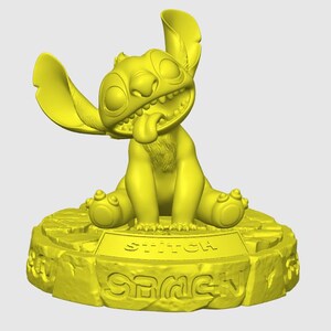 May include: A yellow figurine of the character Stitch from Lilo & Stitch. The figurine is in a sitting position with its tongue sticking out. The base of the figurine has the word "Stitch" and "Game" on it.
