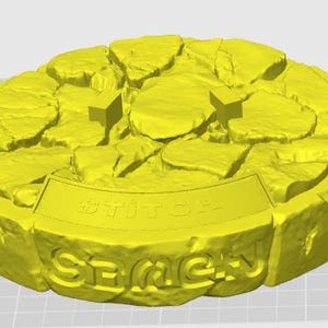 May include: A yellow, circular object with a textured, stone-like appearance. The top surface features irregular shapes, and the side has the word "SEMEH" and "stitch" in raised lettering. Two small, rectangular shapes are on the top surface.