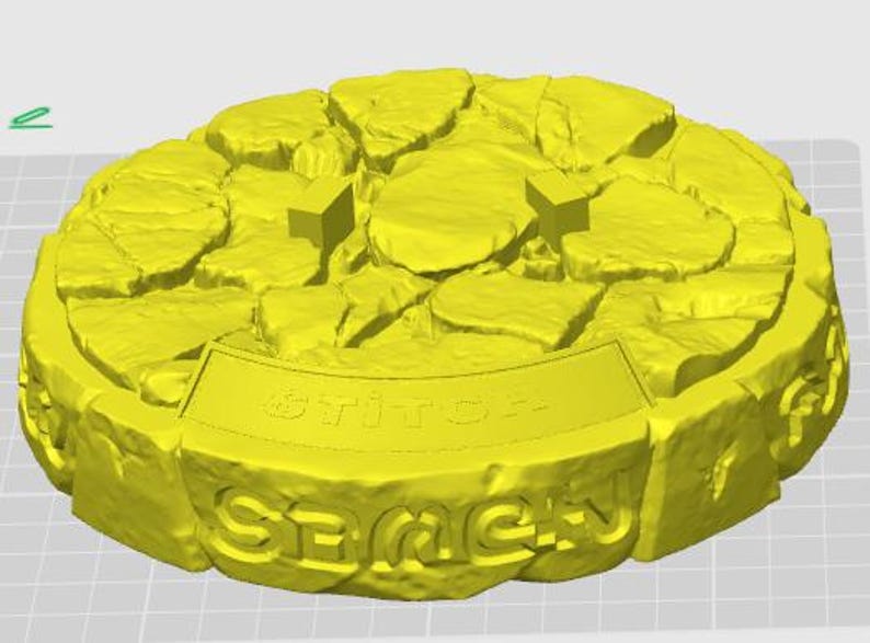 May include: A yellow, circular object with a textured, stone-like appearance. The top surface features irregular shapes, and the side has the word "SEMEH" and "stitch" in raised lettering. Two small, rectangular shapes are on the top surface.
