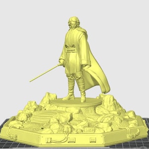 Op de afbeelding: Een geelkleurig beeldje van een personage uit een sciencefictionfranchise, met een lichtzwaard. Het beeldje staat op een rotsachtige, getextureerde basis. De basis is gemonteerd op een rechthoekig platform met gedetailleerde randen.