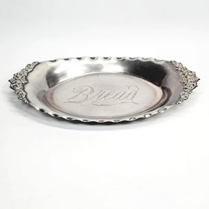 May include: A silver oval bread tray with decorative floral detailing at each end. The word "Bread" is engraved in cursive in the centre. The tray has a scalloped edge.