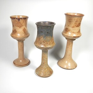 May include: Three ceramic goblets with a flared base and a wide, round bowl. The goblets are glazed in shades of brown, beige, and blue.