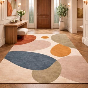 Handmade abstract wool rug with scalloped edges featuring organic shapes in rust, beige, ivory, grey, and charcoal tones on wooden floor in modern living room setting