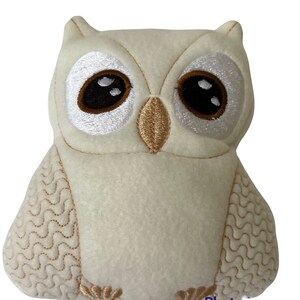 May include: A white plush owl with embroidered brown eyes and a beige beak. The owl has a wavy pattern on its wings and a textured white body.