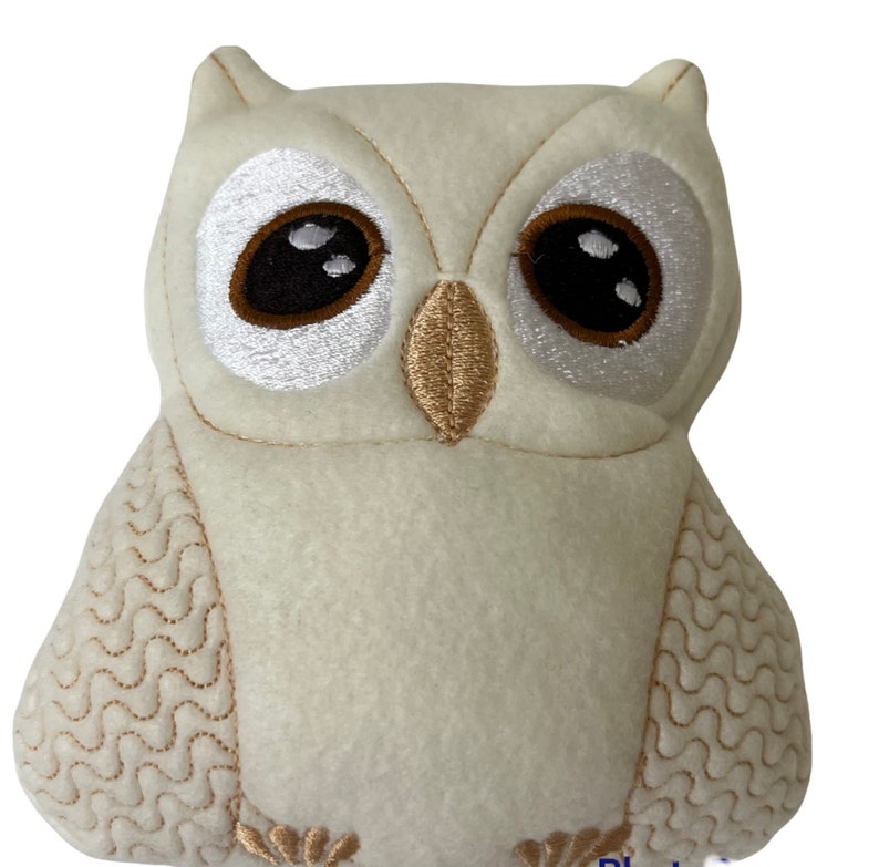 May include: A white plush owl with embroidered brown eyes and a beige beak. The owl has a wavy pattern on its wings and a textured white body.