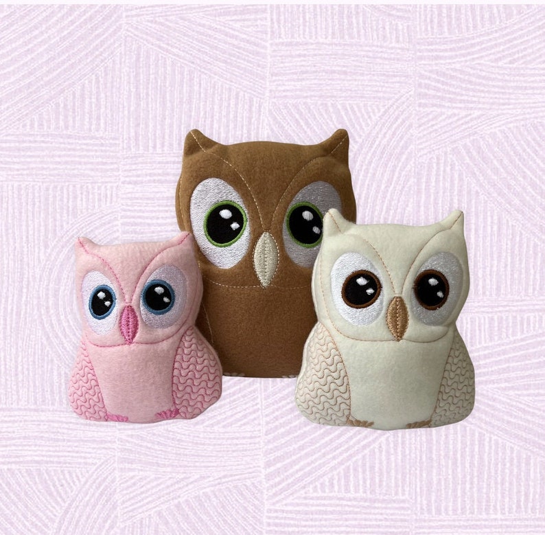 May include: Three plush owl toys, one brown, one white, and one pink. The owls have embroidered eyes and beaks.