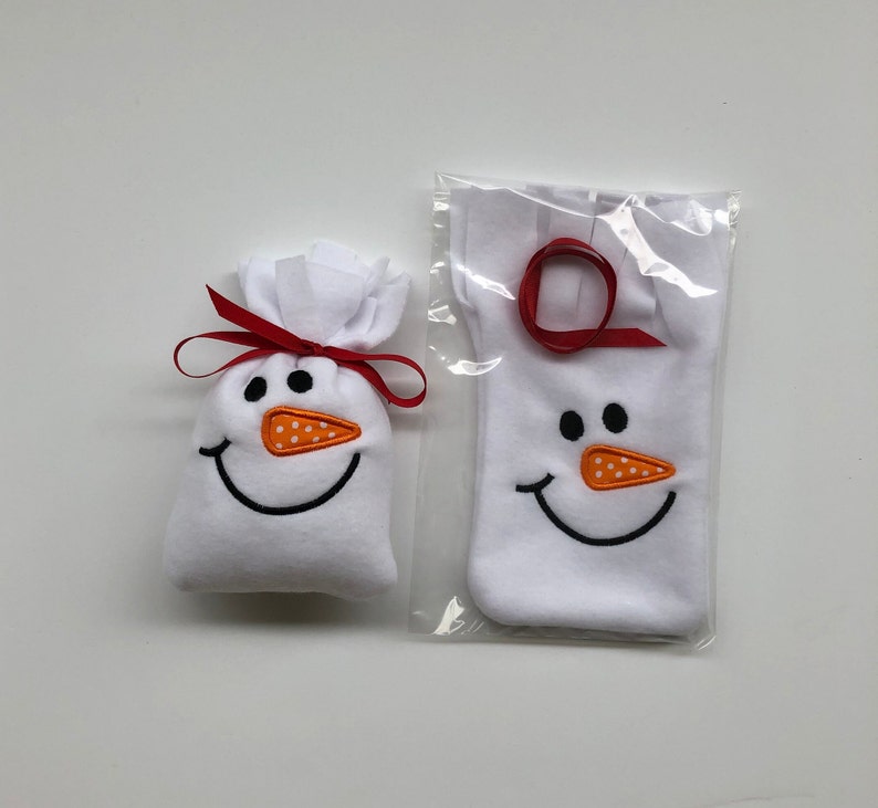 May include: Two white fabric snowman gift bags with red ribbon and orange felt noses. The smaller bag is tied with a red ribbon and the larger bag is in a clear plastic bag.
