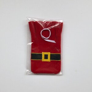 May include: Red felt wine bottle bag with a black belt and gold buckle, resembling Santa Claus. The bag is packaged in a clear plastic bag with a white ribbon.