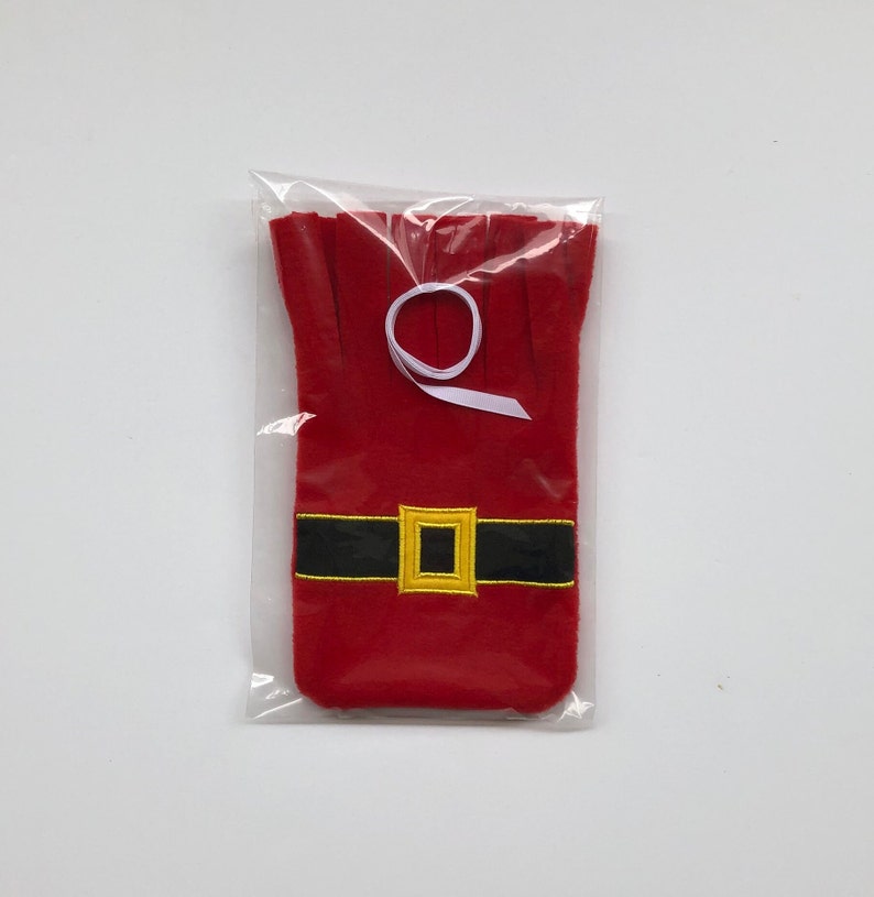 May include: Red felt wine bottle bag with a black belt and gold buckle, resembling Santa Claus. The bag is packaged in a clear plastic bag with a white ribbon.