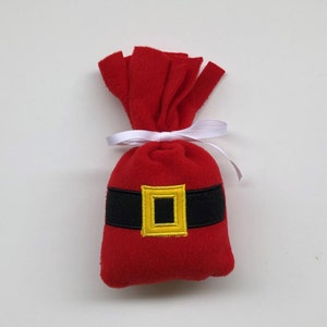 May include: A red felt Santa sack with a black belt and a gold buckle. The sack is tied with a white ribbon.