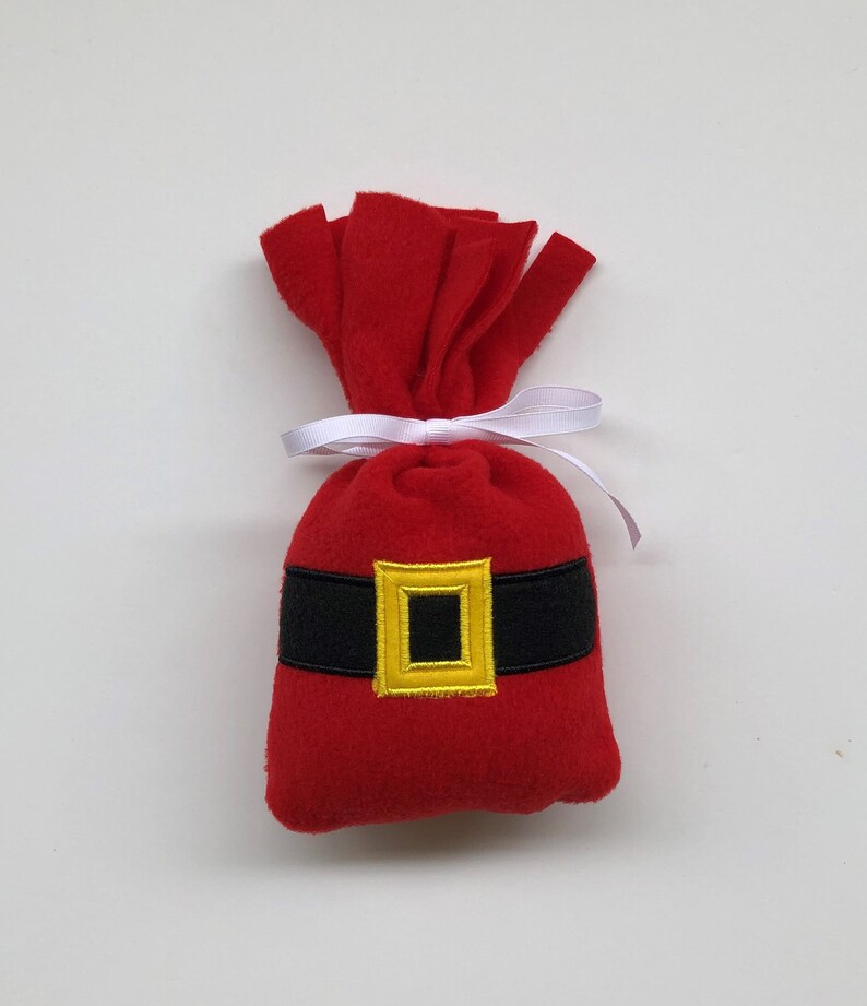 May include: A red felt Santa sack with a black belt and a gold buckle. The sack is tied with a white ribbon.