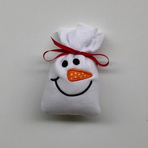 May include: White fabric snowman gift bag with a red ribbon and an orange felt nose with white polka dots.