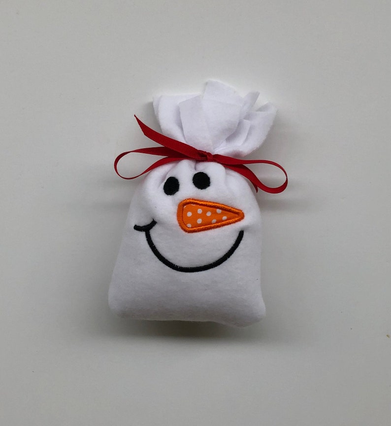 May include: White fabric snowman gift bag with a red ribbon and an orange felt nose with white polka dots.