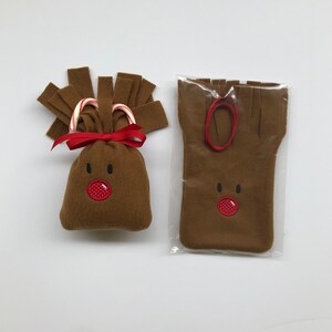 May include: A brown felt reindeer gift bag with a red nose and candy cane antlers. The bag is packaged in a clear plastic bag with a red ribbon.