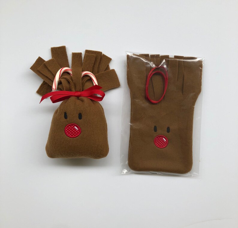 May include: A brown felt reindeer gift bag with a red nose and candy cane antlers. The bag is packaged in a clear plastic bag with a red ribbon.