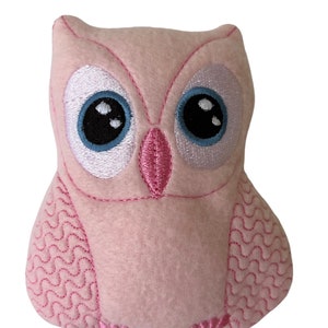 May include: A pink plush owl with embroidered eyes, beak, and feathers. The owl has a light blue and white eye with a black pupil.