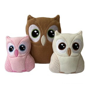 May include: Three plush owl toys, one brown, one white, and one pink. The owls have embroidered eyes and beaks.