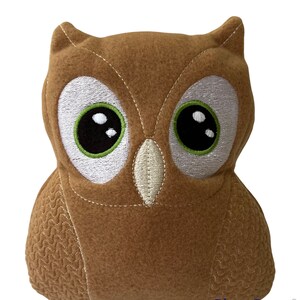 May include: A brown plush owl with large, embroidered eyes. The owl has a stitched beak and a textured pattern on its body.