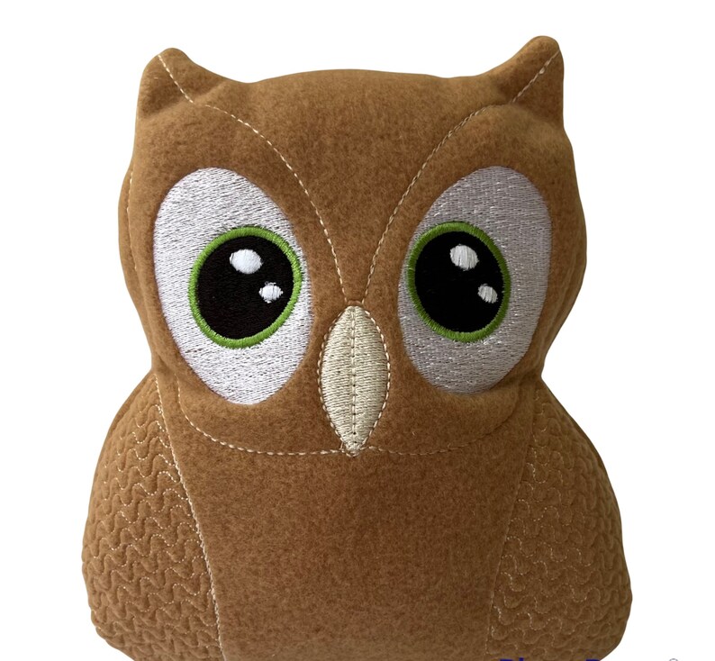May include: A brown plush owl with large, embroidered eyes. The owl has a stitched beak and a textured pattern on its body.
