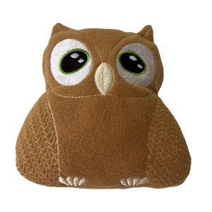 May include: A brown plush owl with embroidered eyes and a textured pattern. The owl has a white beak and white feet.