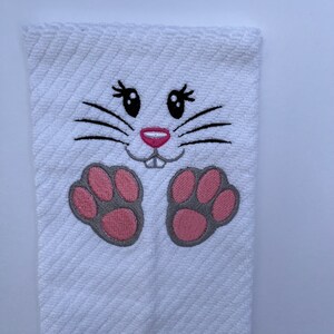 May include: White kitchen towel with an embroidered bunny face and pink paw prints.
