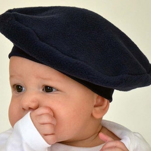 May include: A navy blue fleece beret for a baby. The beret is soft and comfortable, and it is perfect for keeping a baby's head warm.