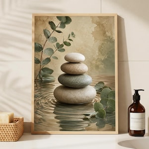 May include: A framed print showing a stack of smooth stones in water, with eucalyptus leaves. The artwork has a neutral colour palette of greens, browns, and beige. The print is displayed on a white surface with a soap dish and a soap dispenser.