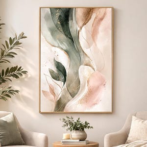 May include: Abstract watercolor art print in a gold frame. The artwork features flowing shapes in shades of green, pink, and beige, with gold accents. The painting is displayed in a living room setting with two armchairs and a small wooden table.