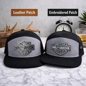 May include: Two black and gray Harley-Davidson trucker hats. Each hat features a gray front panel with the Harley-Davidson logo and the words "MOTOR HARLEY-DAVIDSON CYCLES". One hat has a leather patch, the other an embroidered patch.