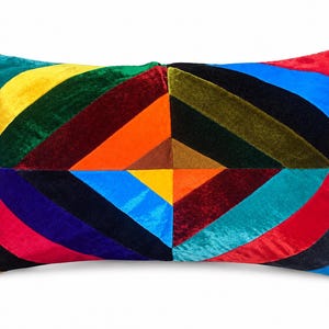 May include: A rectangular velvet throw pillow featuring a vibrant geometric pattern of diagonal stripes in shades of red, orange, yellow, green, blue, purple, and black, arranged in a symmetrical design that meets at the center of the pillow.