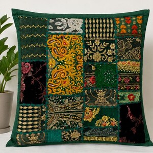 Puede incluir: Una funda de cojín decorativa cuadrada con un diseño de patchwork de varios paneles de tela en verde, negro y dorado. La superficie está adornada con intrincados bordados dorados, motivos florales, diseños de cachemira y pequeñas cuentas.