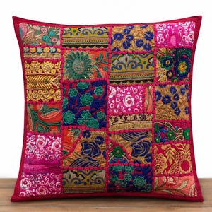 Puede incluir: Una funda de cojín cuadrada con un diseño de patchwork de varios cuadrados de tela bordados en tonos vibrantes de rosa, naranja, azul, verde y dorado. Los paneles de tela individuales están unidos por costuras rosas en relieve.