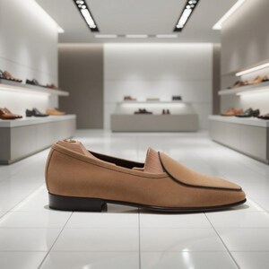May include: A tan suede loafer with a black sole and trim, displayed in a well-lit shoe store. The shoe has a classic design with a pointed toe. Other shoes are visible on shelves in the background.