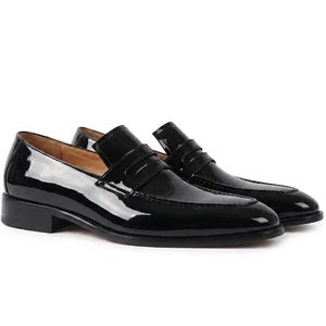 May include: A pair of black patent leather penny loafers. These smart slip-on shoes have a low heel and a high-shine finish. The shoes are designed for comfort and style, suitable for various occasions. The shoes are approximately 28 cm in length.