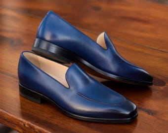 May include: A pair of blue leather loafers with a classic design. The shoes have a low heel and a smooth, polished finish. The loafers are displayed on a wooden surface.
