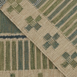 May include: Close-up of a woven rug with a geometric pattern. The rug features a combination of blue, green, and beige tones. The design includes stripes and cross-like shapes, creating a textured and patterned surface.