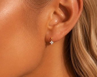 May include: A small gold earring featuring a delicate four-petalled flower design. The centre of the flower is adorned with a tiny, clear, sparkling gemstone. The earring is attached to a thin gold post that secures it to the earlobe.
