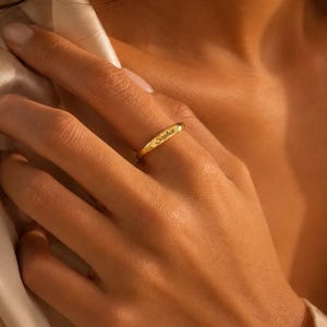 May include: A polished gold band ring featuring a smooth, rounded surface with the name Sophia engraved in a delicate script font. The ring has a warm, metallic luster and a simple, continuous circular design that sits on the finger.