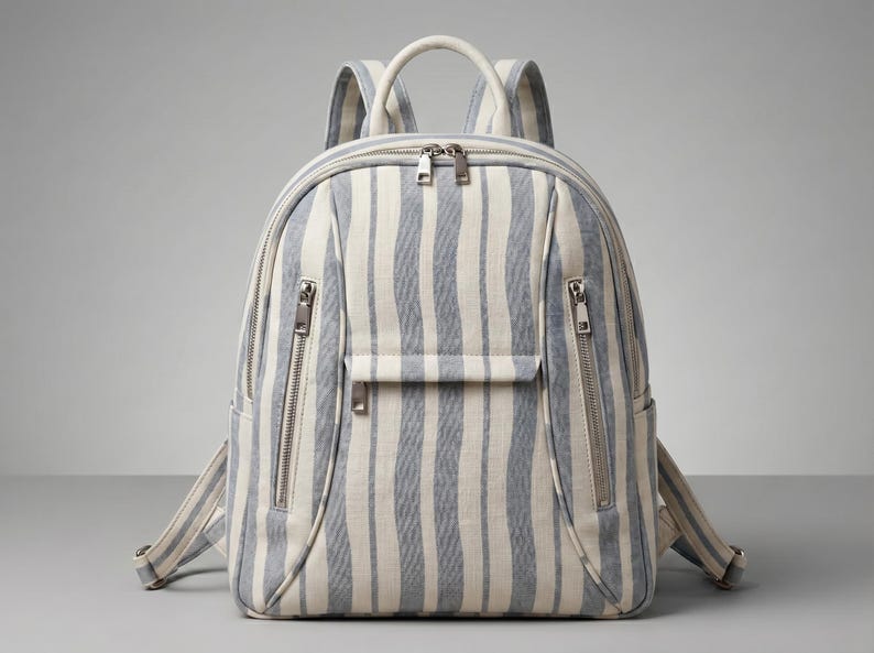 K&ouml;nnte beinhalten: Ein gestreifter Rucksack mit einem hellblau-wei&szlig;en vertikalen Muster. Die Tasche hat einen oberen Griff, verstellbare Tr&auml;ger und mehrere Rei&szlig;verschlussf&auml;cher. Die Rei&szlig;verschl&uuml;sse und Beschl&auml;ge sind silberfarben.