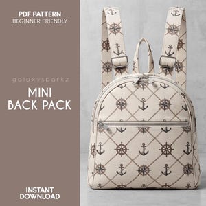 May include: A mini backpack featuring a cream-colored fabric with a repeating nautical pattern of brown anchors, ship wheels, and compasses connected by diagonal rope lines. The bag has a top handle, two shoulder straps, and a front zipper pocket.
